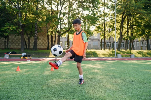 Motivated teen football player stuffs soccer ball on leg. Practicing sport exercises at artificial stadium. — Stock Photo, Image