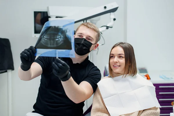 高い資格を持つ歯科医は、若い女性患者に現代のクリニックで歯科椅子の歯のX線を示しています. — ストック写真