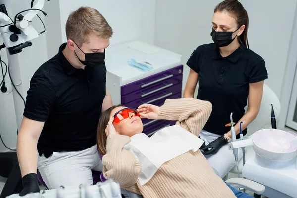 Bela paciente feminina em óculos de proteção vermelhos em uma cadeira dentária na moderna clínica elegante. — Fotografia de Stock