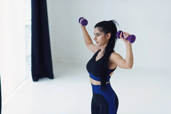 Jovem mulher bonita fazendo exercícios com halteres no estúdio de fitness. Menina atlética desfrutando de seu processo de treinamento. — Fotografia de Stock