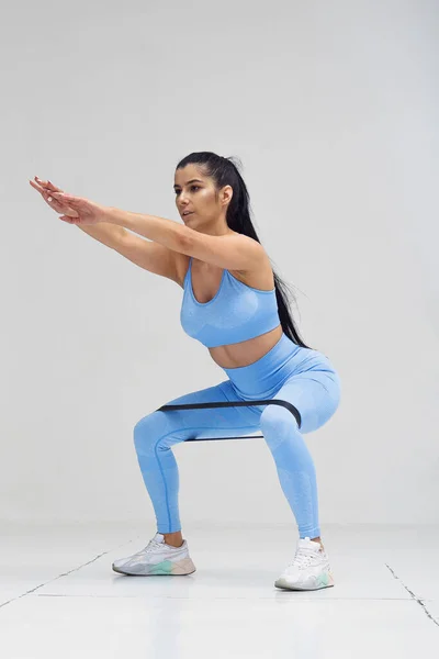 Mujer deportiva en ropa de moda en cuclillas con banda de resistencia de fitness. concepto de estilo de vida saludable. — Foto de Stock