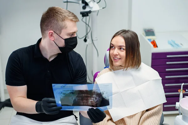 高い資格を持つ歯科医は、若い女性患者に現代のクリニックで歯科椅子の歯のX線を示しています. — ストック写真