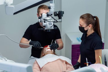 Siyah lateks eldivenli dişçi dişçi dişçi dişçi dişlerini tedavi ederken diş mikroskobuna bakar..