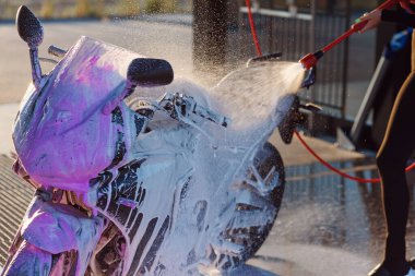 Güzel bir kız oto yıkamada motosikleti yüksek basınçlı suyla yıkıyor..