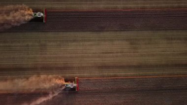 Bir tarlada çalışan modern hasatçıların hava görüntüsü. Gün batımında tarlada buğday hasadını birleştirir..