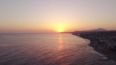 Bir İHA gün doğumunda Ege Denizi sahilinde adanın üzerinde uçar..