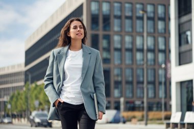 Dışarıda dizüstü bilgisayarı ve defteri olan takım elbiseli güzel bir iş kadını. Esmer beyaz kadın, ofisin yanında duruyor..