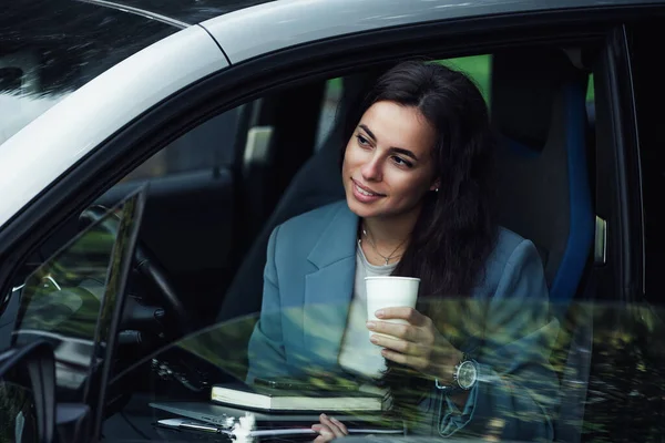 Uma jovem atraente a fazer uma pausa para o café. Empresária de sucesso com laptop, notebook e smartphone sentado no carro. — Fotografia de Stock