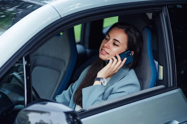 Çekici genç bir kadın arabada otururken cep telefonuyla konuşur. Genç bir iş kadınının portresi.