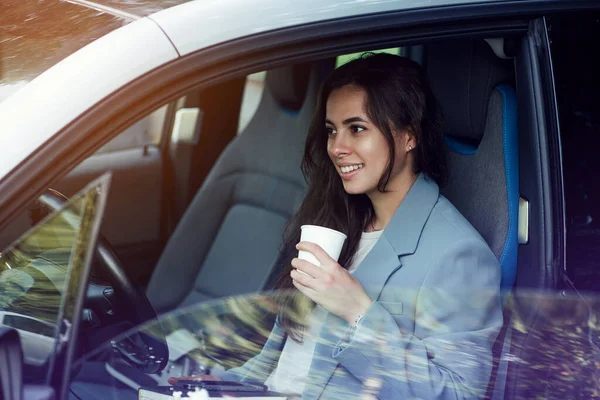 Uma jovem atraente a fazer uma pausa para o café. Empresária de sucesso com laptop, notebook e smartphone sentado no carro. — Fotografia de Stock