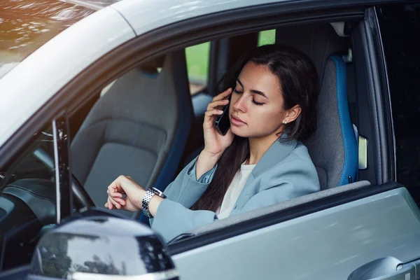 Jovem atraente fala no telefone celular enquanto está sentado no carro. Retrato de uma jovem mulher de negócios. — Fotografia de Stock