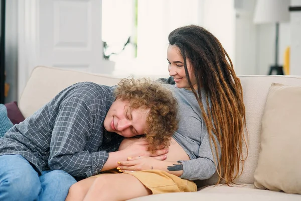 Echtgenoot aanraken zwangere buik van zijn charmante vrolijke vrouw die op de bank in gezellige woonkamer — Stockfoto