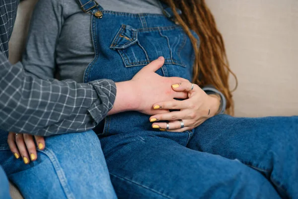 Σύζυγος αγγίζοντας έγκυος κοιλιά του γοητευτικό χαρούμενη γυναίκα του που βρίσκεται στον καναπέ στο άνετο σαλόνι — Φωτογραφία Αρχείου