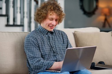 Kanepede oturan ve tableti elinde tutan kıvırcık saçlı genç hippi..