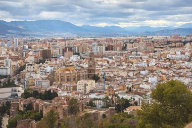Büyük bir katedrali olan tarihi bir İspanyol şehrinin panoramik manzarası yoğun şehir binaları ve bulutlu bir gökyüzünün altındaki uzak dağlarla çevrili. Eski ve modern mimarinin karışımı şehirlerin zengin kültürel ve mimari mirasını ön plana çıkarıyor