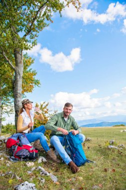Genç çift dağlarda seyahat ederken kayanın üzerinde dinlenirken su içiyor.