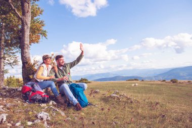 Genç çift dağlarda seyahat ederken kayanın üzerinde dinlenirken su içiyor.