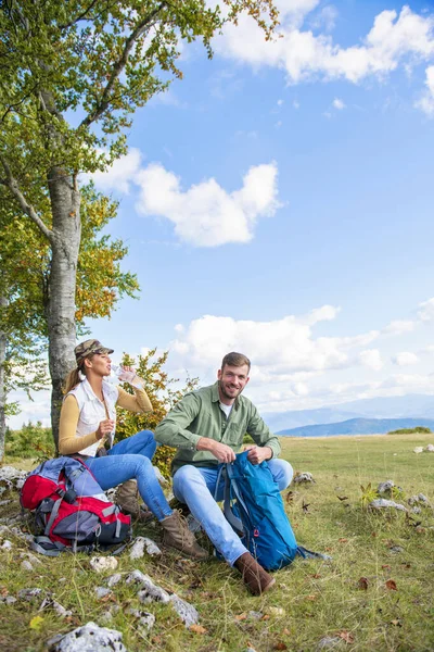 Genç çift dağlarda seyahat ederken kayanın üzerinde dinlenirken su içiyor.