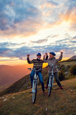 Parkta bisiklet süren ve el kaldıran mutlu yaşlı çift.