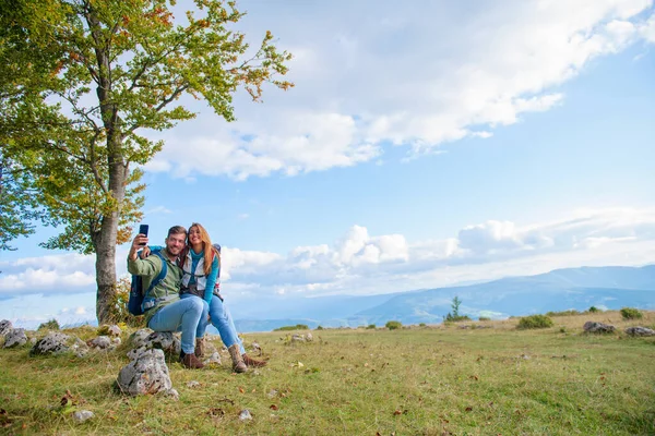 Pareja sentada en una roca descansando durante la caminata y tomando selfie — Foto de Stock