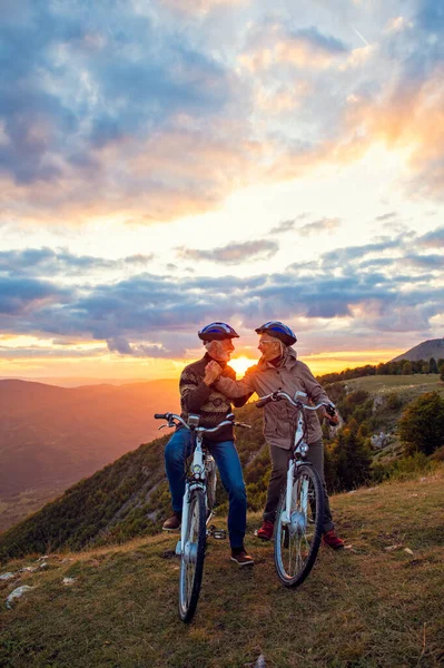 Pareja de ancianos con bicicletas de pie en el parque de montaña besándose —  Fotos de Stock