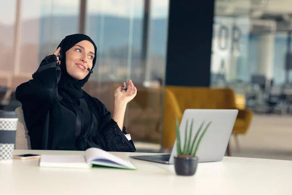 Heureuse femme d'affaires musulmane en hijab au bureau. Femme arabe souriante travaillant sur un ordinateur portable et parlant sur un smartphone — Photo