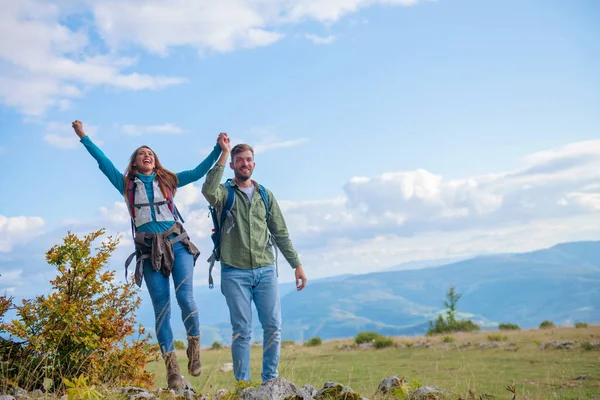Lyckliga resenärer par erövrade toppen av berget, höjer händerna — Stockfoto