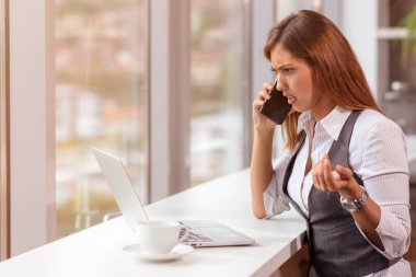 Bilgisayarlı ve akıllı telefonlu genç bir kadın ofiste çalışıyor..