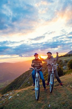 Parkta bisiklet süren ve el kaldıran mutlu yaşlı çift.