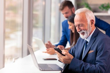 Üst düzey yönetici arka planda genç dilleri olan bir cep telefonu kullanıyor