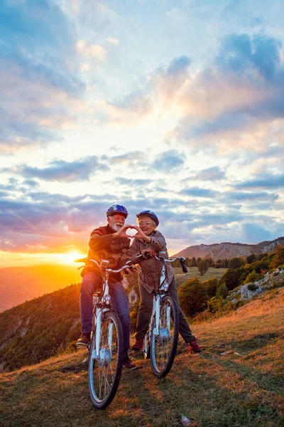 Pareja mayor activa en bicicletas haciendo forma de corazón con las manos y besándose. —  Fotos de Stock