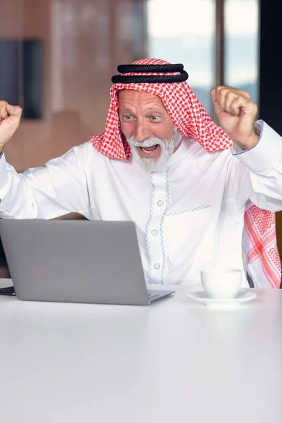 Empresário árabe comemorando vitória no escritório usando laptop. — Fotografia de Stock