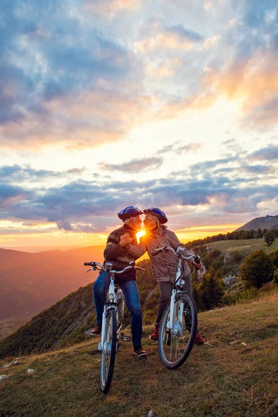 Pareja de ancianos con bicicletas de pie en el parque de montaña besándose —  Fotos de Stock