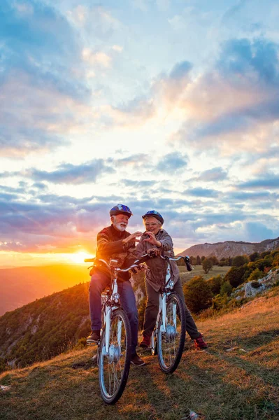 Pareja mayor activa en bicicletas haciendo forma de corazón con las manos y besándose. —  Fotos de Stock