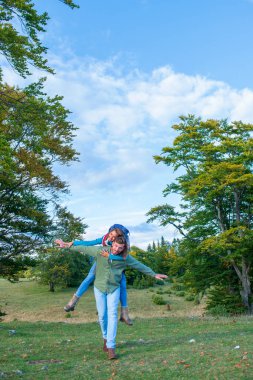 Sırt çantalı mutlu çift dağlık arazide geziyor. Erkek arkadaşı kız arkadaşını sırtında taşıyor..