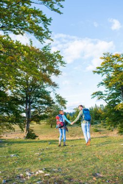 Yeşil çayırlarda sırt çantalarıyla yürüyen güzel bir çift yaz boyunca yüksek dağlarda seyahat ediyor. Arka görünüm