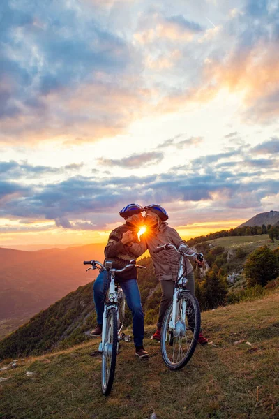 Elderly couple with bicycles standing at the mountain park kissing — Stock Photo, Image