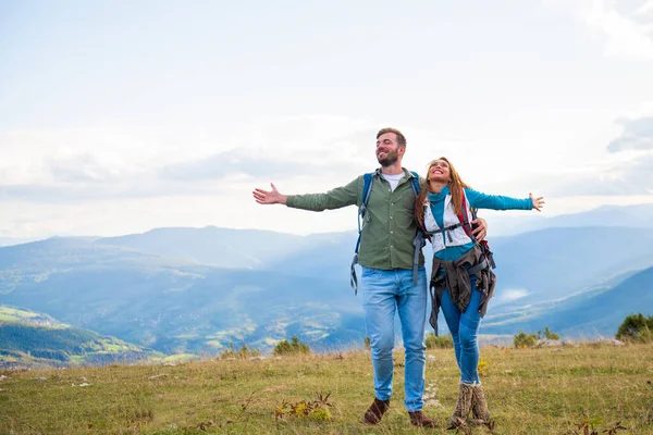 Viajeros felices pareja conquistó la cima de la montaña, levanta las manos — Foto de Stock