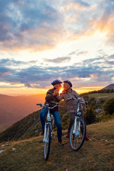 Pareja de ancianos con bicicletas de pie en el parque de montaña besándose —  Fotos de Stock