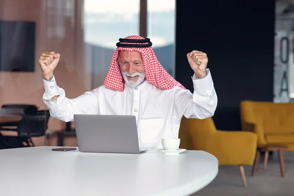 Empresário árabe comemorando vitória no escritório usando laptop. — Fotografia de Stock