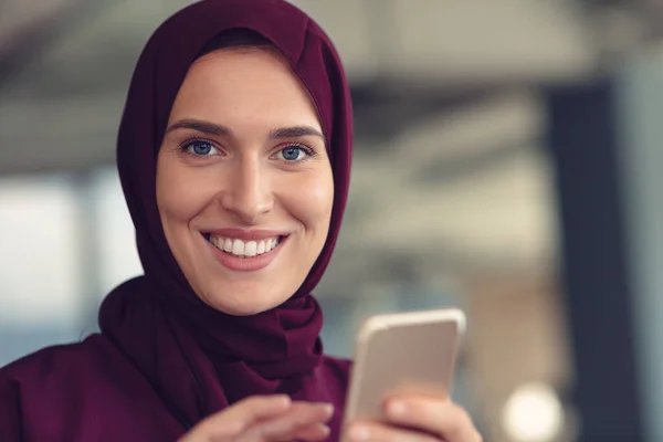 Boldog muszlim üzletasszony hidzsábban az irodában. Mosolygó arab nő dolgozik laptop és használja a szmatphone. — Stock Fotó