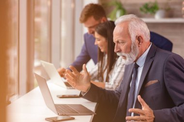 Üst düzey yönetici arka planda genç dilleri olan bir dizüstü bilgisayar kullanıyor.