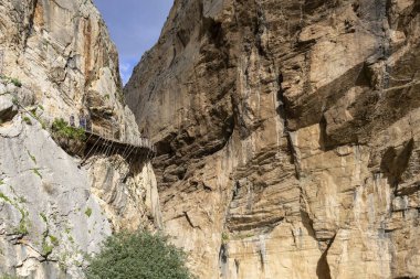 İnsanlar İspanya 'da Caminito del Rey yolunda yürüyor. Yol, kayalık duvarlar ve yeşilliklerle çevrili dik uçurumlara karşı inşa edilmiştir. Açık bir gökyüzünün altında..