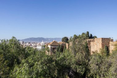 Ziyaretçiler Malaga, İspanya 'da Alkazaba' yı keşfediyorlar. Sahne, şehir manzaralı yeşil ağaçların arasındaki antik duvarları ve mavi gökyüzünün altındaki uzak dağları gösteriyor..