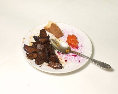 Kirli beyaz bir tabakta yemek artıkları hafif bir arka planda çatal bıçak takımı.