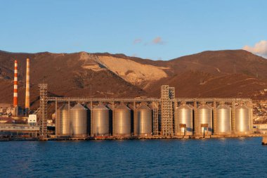 Dağın arka planına karşı denizdeki limanda tahıl depolamak için sarnıçlar