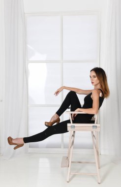 Moda pozu. Kadın sandalyede yüksek topuklularla oturuyor.