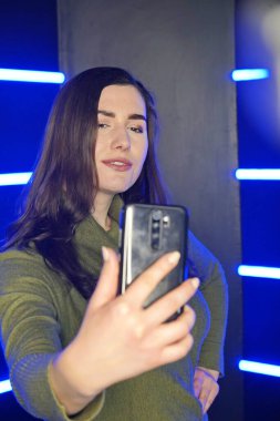 Kız telefonda arka planda neon ışıklı selfie çekiyor.