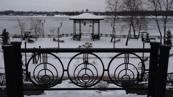 Park onder sneeuw tegen de achtergrond van de bevroren rivier, eenzame persoon loopt langzaam — Stockvideo