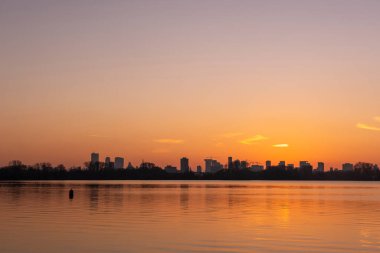 Kralingse Plas 'tan (Kralingen Gölü) görüleceği gibi Rotterdam ufuk çizgisinde gün batımı gölün durgun sularına yansıyan renkli gökyüzü